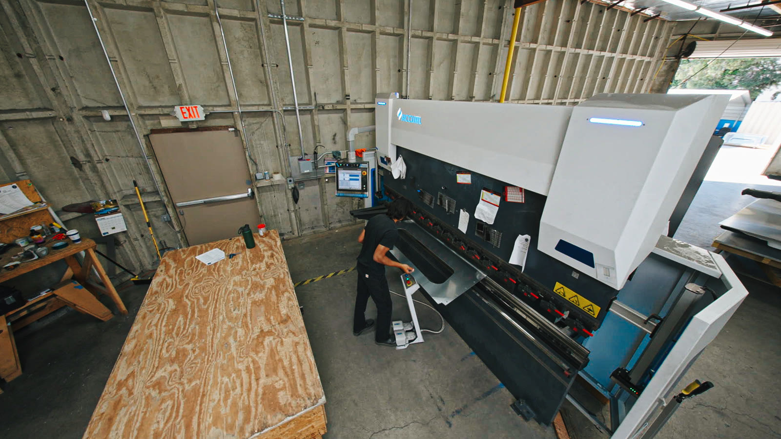 The large white-and-black bending machine seen from above with the plywood workbench in front.