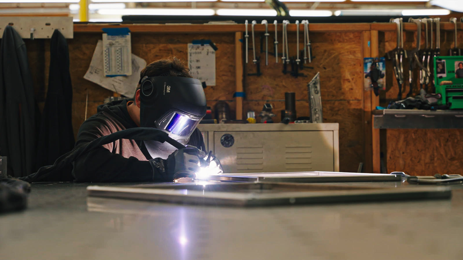 A bright welding arc seen through the opening of a low silver rectangular frame.
