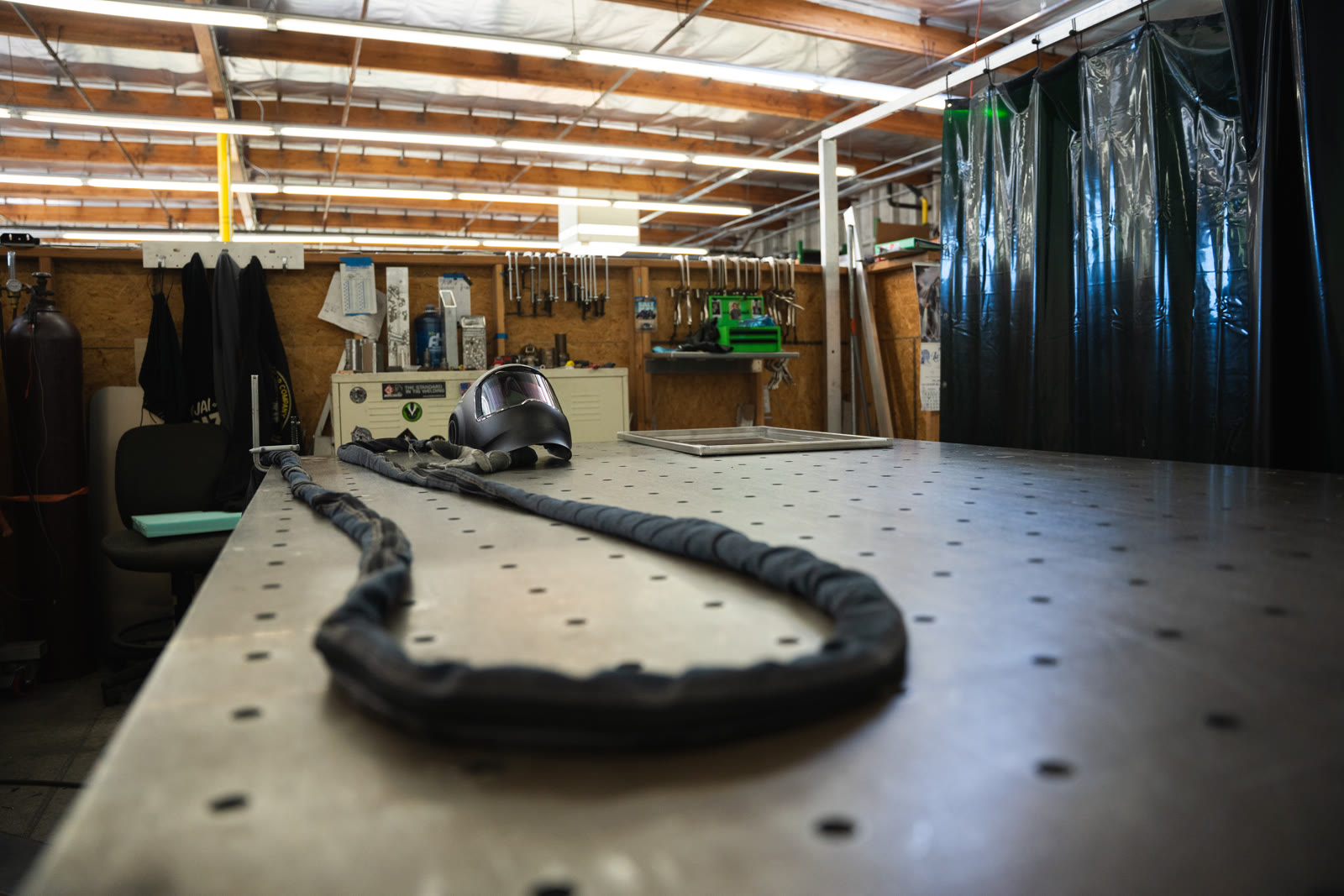 A dark coiled cable or hose resting on a perforated metal worktable in the welding area.