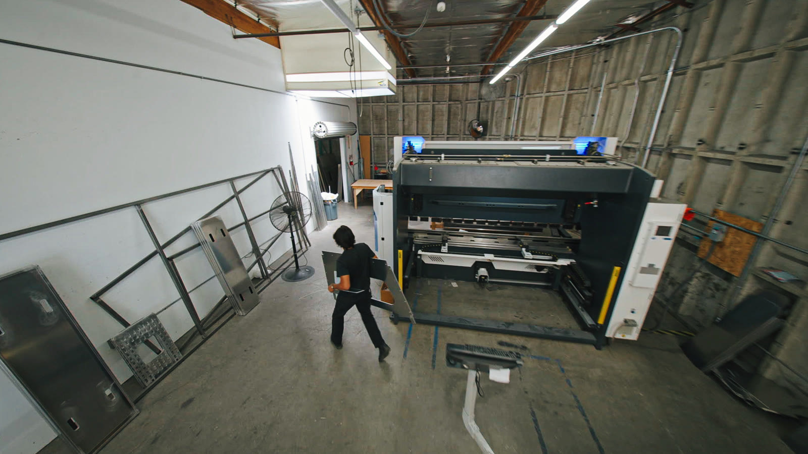 The press brake and surrounding tables seen from above, with a worker crossing the open floor.