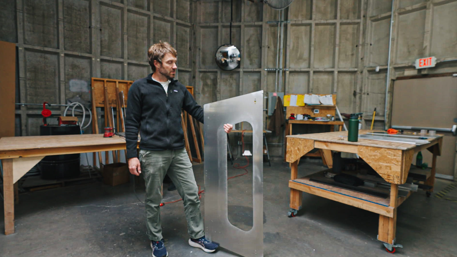 A worker standing with a tall silver panel containing two rectangular openings in the factory work area.