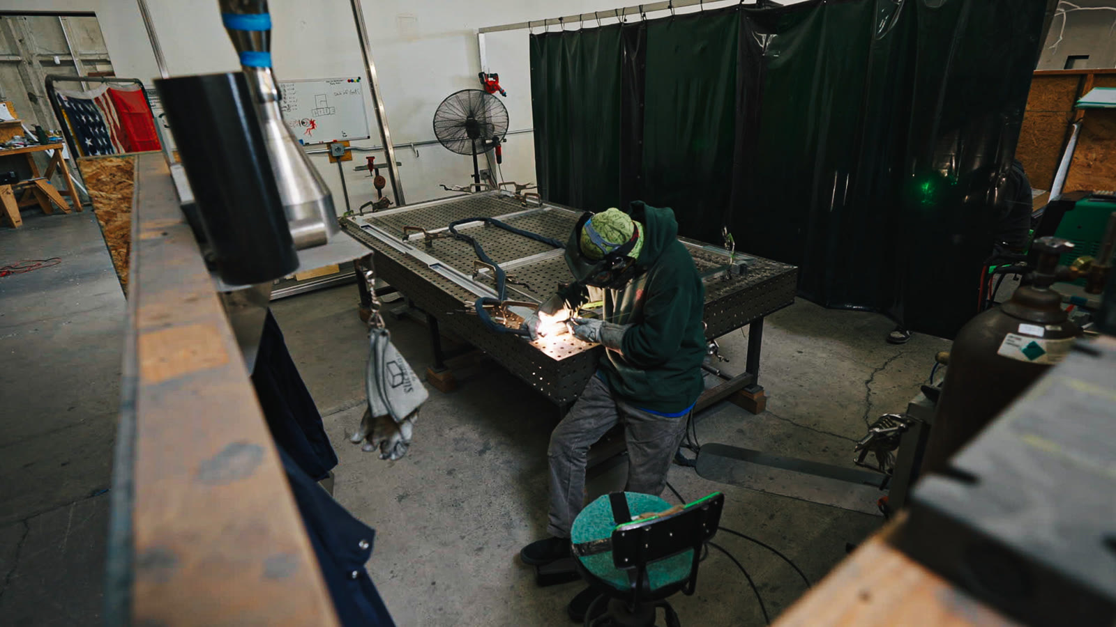 A technician welding a metal frame on the large perforated table, seen from above the station.