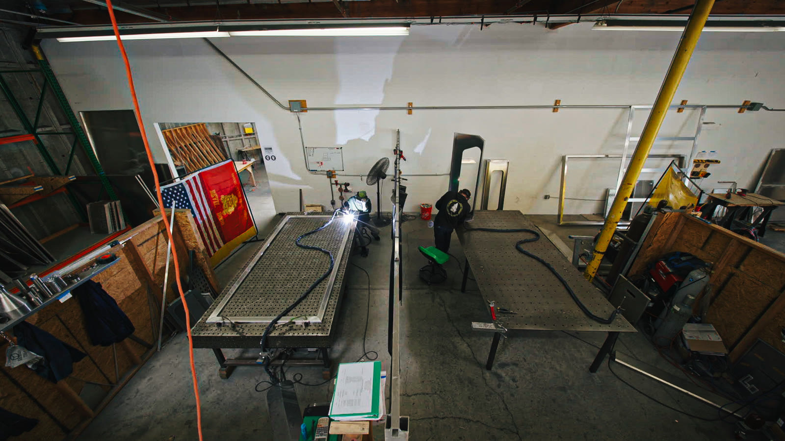 Two long perforated worktables, welding leads, and fabrication equipment seen from above.