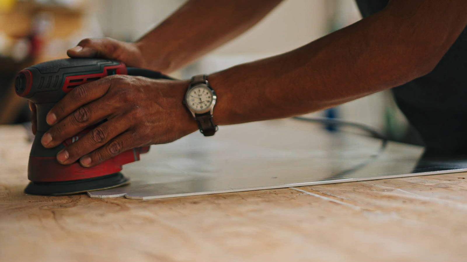 Close view of two hands guiding a round power sander across a flat silver sheet.